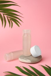 Photo of Cosmetic products, stone and palm leaves on pink background