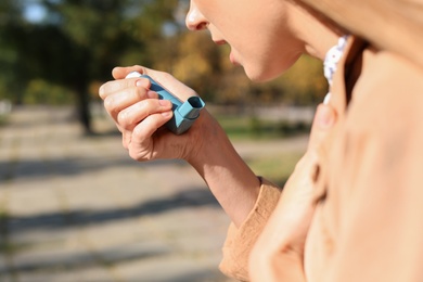 Woman using asthma inhaler outdoors. Health care