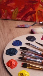 Photo of Artist's palette with many colorful paints and brushes on wooden table, closeup