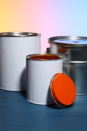 Photo of Cans and bucket of orange paint on blue wooden table against color background