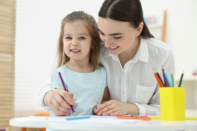 Photo of Mother and her little daughter drawing with colorful pencils at home