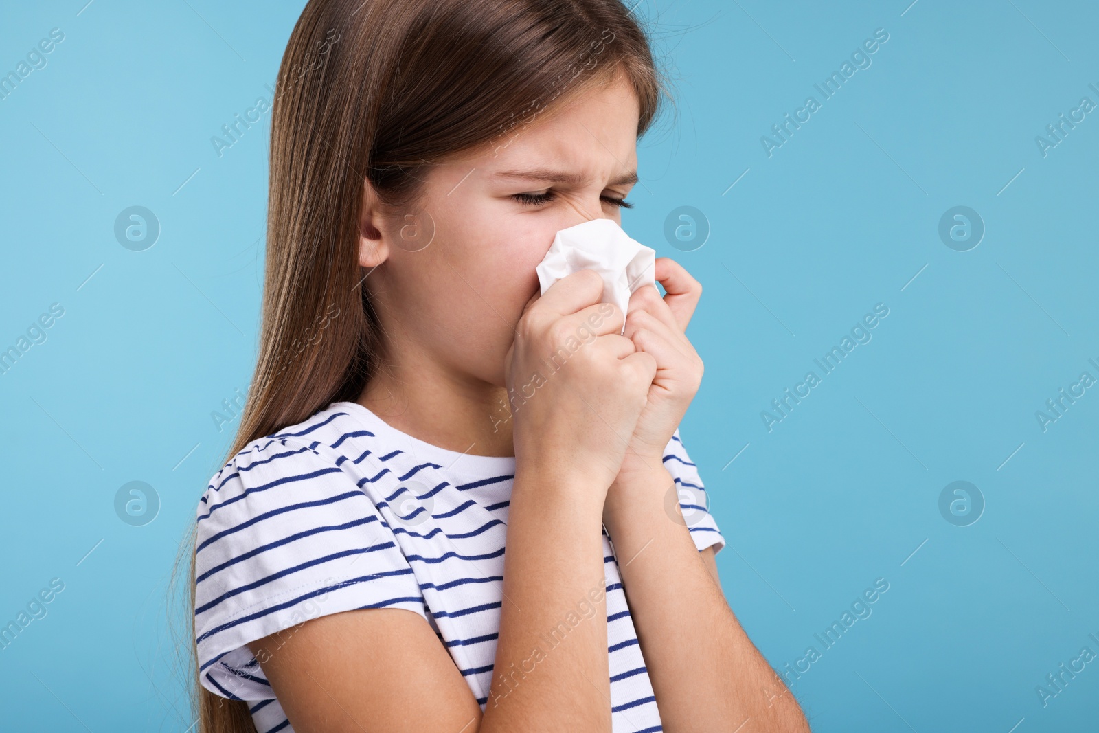 Photo of Sick girl with tissue coughing on light blue background