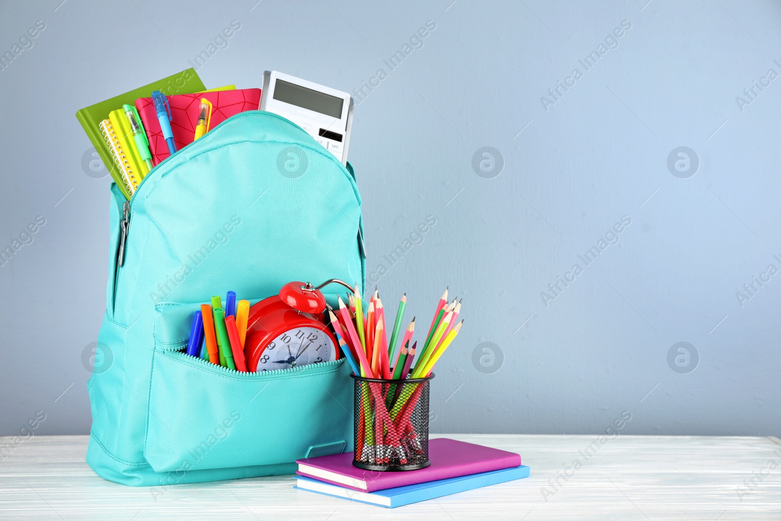Photo of Bright backpack with school stationery on white wooden table against light background, space for text