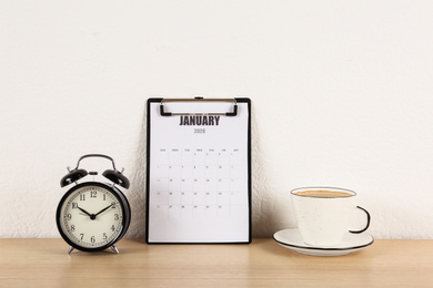 Photo of Calendar, alarm clock and cup of coffee on wooden table