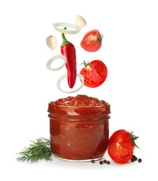 Image of Different ingredients falling into glass jar with delicious adjika sauce on white background