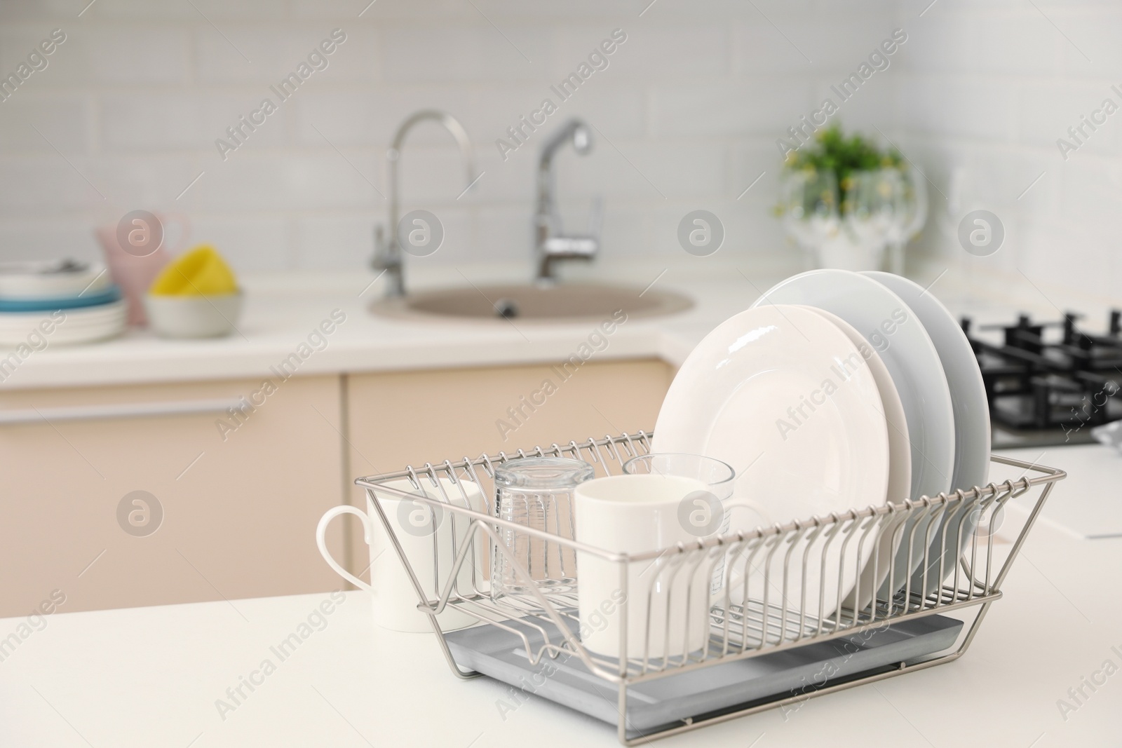 Photo of Dish drainer with clean dinnerware on table in kitchen. Space for text