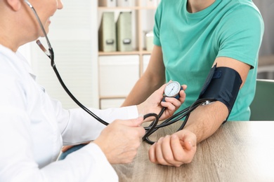 Man visiting doctor in hospital, closeup. Measuring blood pressure and checking pulse