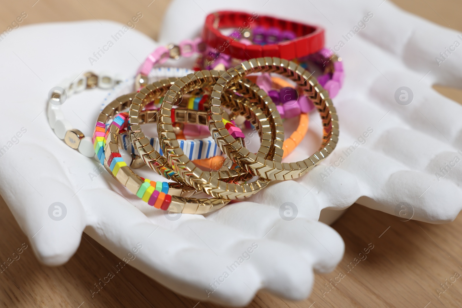 Photo of Ceramic hand stand with many different bracelets on wooden table, closeup