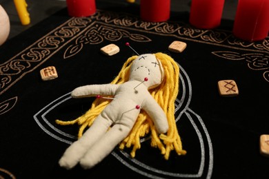 Voodoo doll pierced with pins and runes on black mat. Curse ceremony