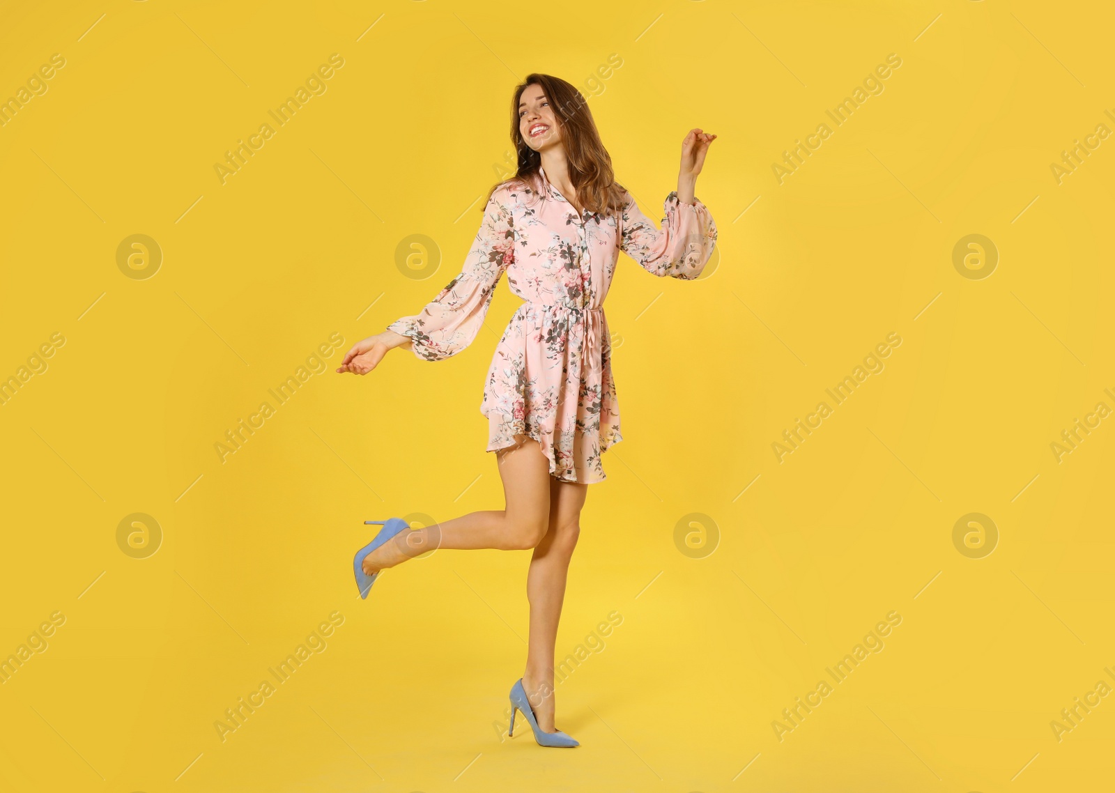 Photo of Young woman wearing floral print dress and elegant shoes on yellow background