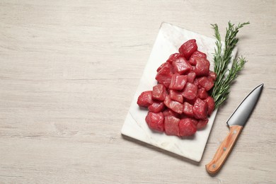 Photo of Cooking delicious goulash. Raw beef meat, rosemary and knife on white wooden table, flat lay. Space for text