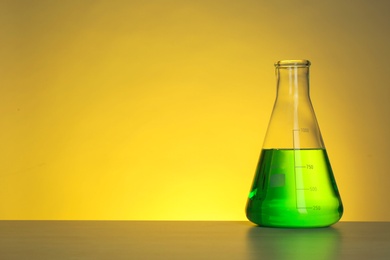 Conical flask with liquid on table against color background. Chemistry laboratory glassware