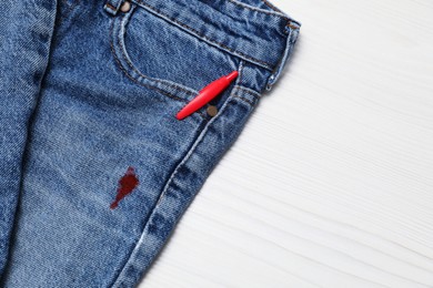 Jeans with stain of red ink and pen in pocket on wooden table, top view. Space for text