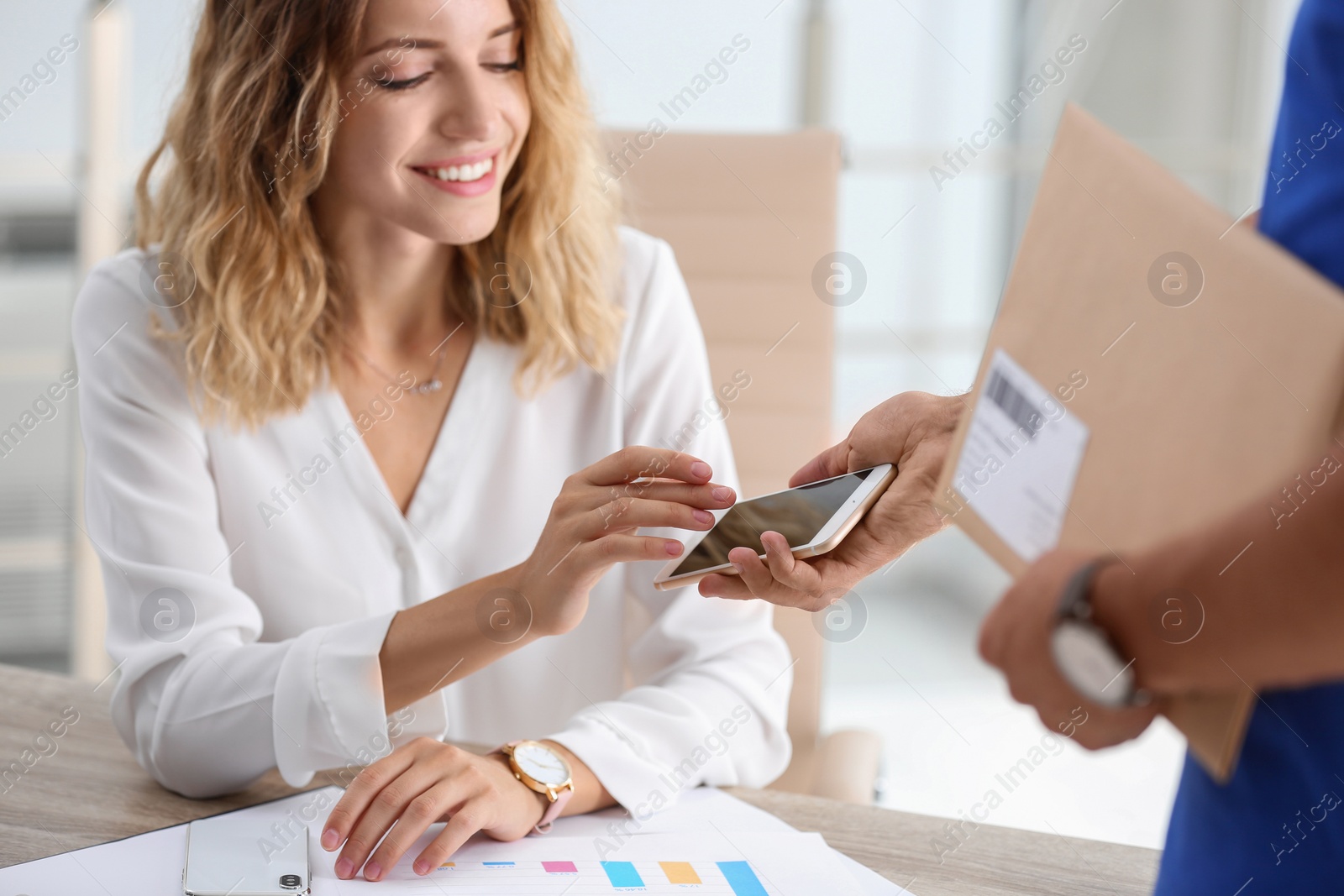 Photo of Woman using smartphone app to confirm receipt of envelope from courier in office