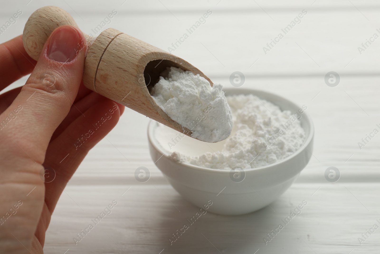 Photo of Woman taking baking powder with scoop from bowl at white wooden table, closeup