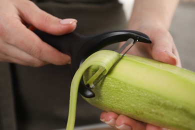 Woman peeling fresh zucchini in kitchen, closeup