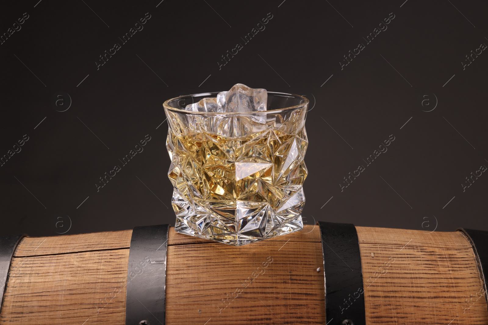 Photo of Whiskey in glass on wooden barrel against dark background