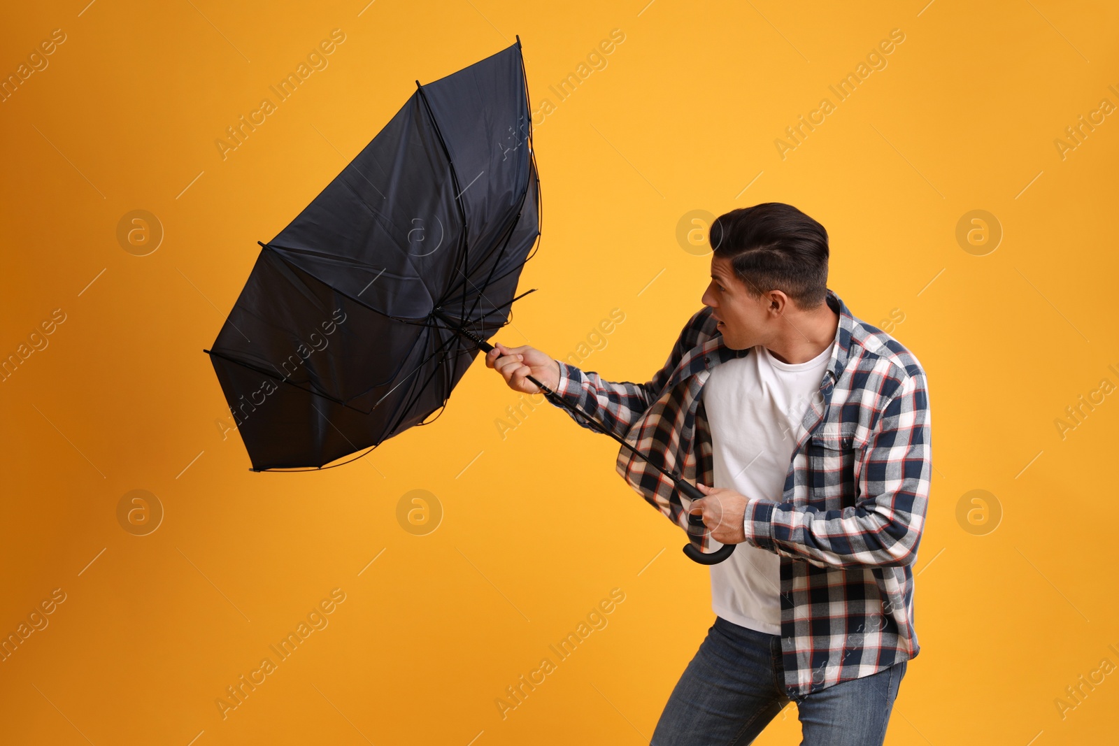 Photo of Man with umbrella caught in gust of wind on yellow background