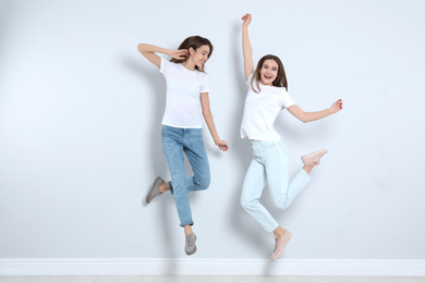 Young women in stylish jeans jumping near light wall