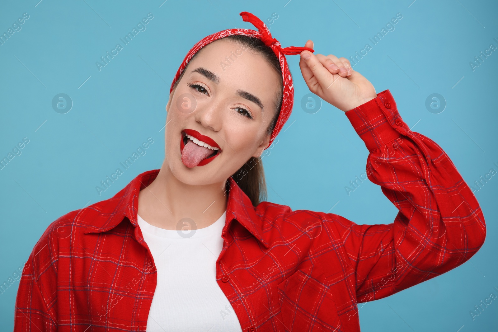 Photo of Happy woman showing her tongue on light blue background