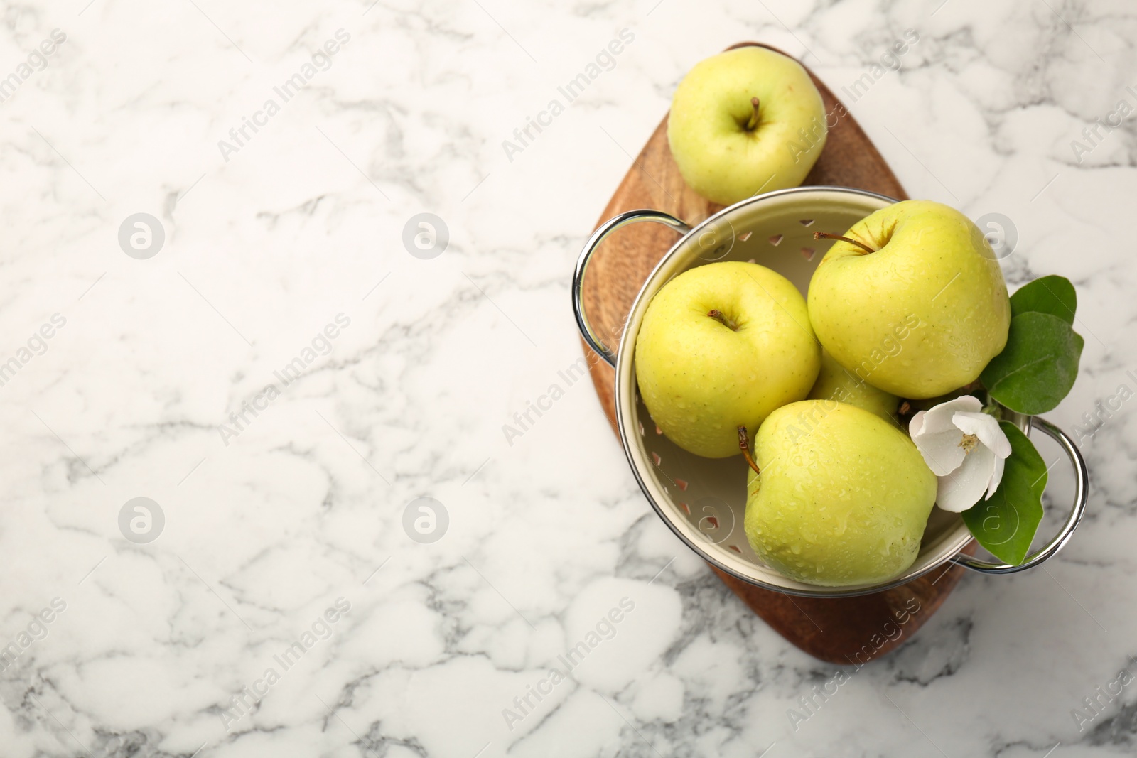 Photo of Colander with fresh apples and beautiful spring blossom on white marble table, top view. Space for text