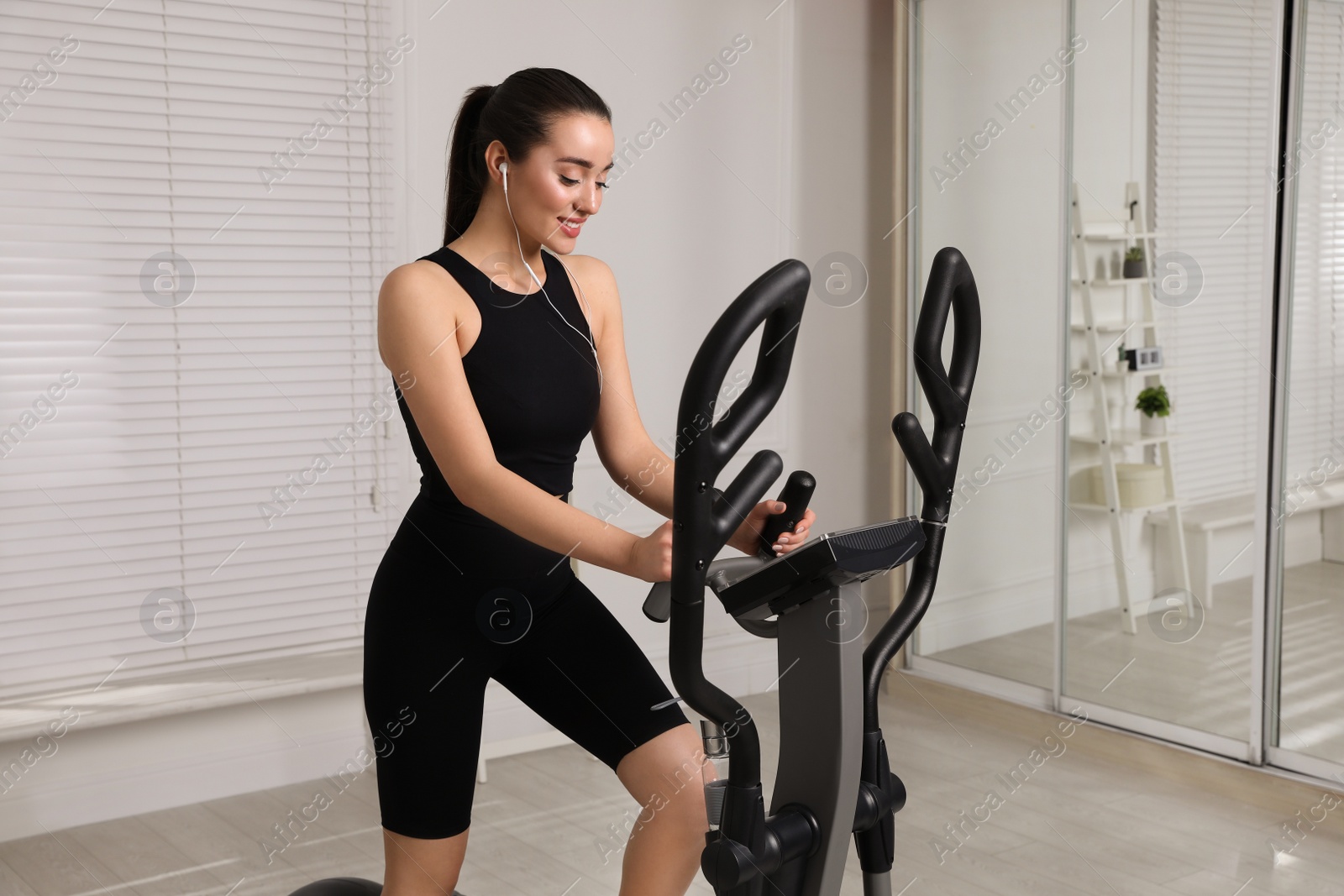 Photo of Happy young woman training on elliptical machine at home