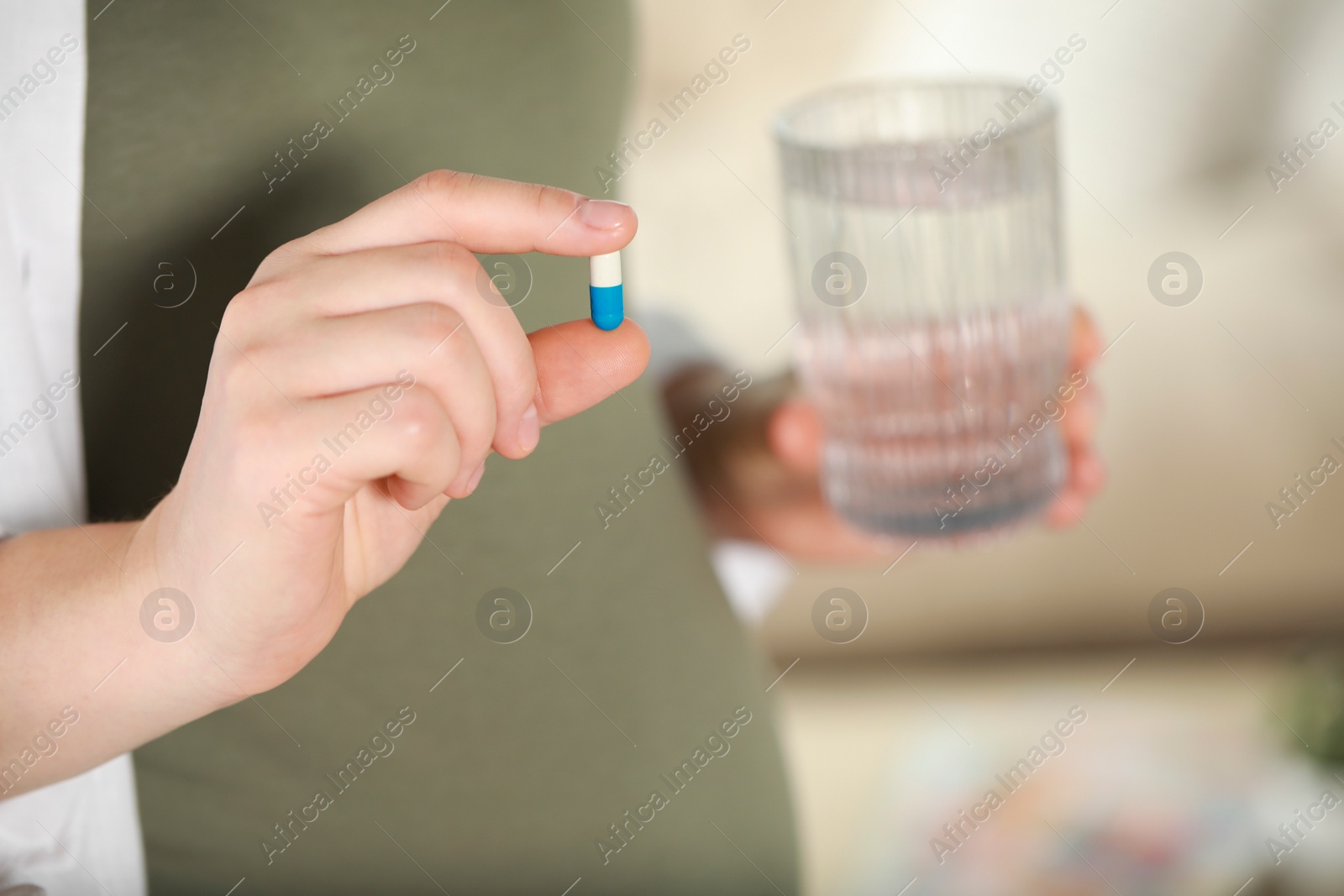 Photo of Pregnant woman holding pill and glass of water indoors, closeup