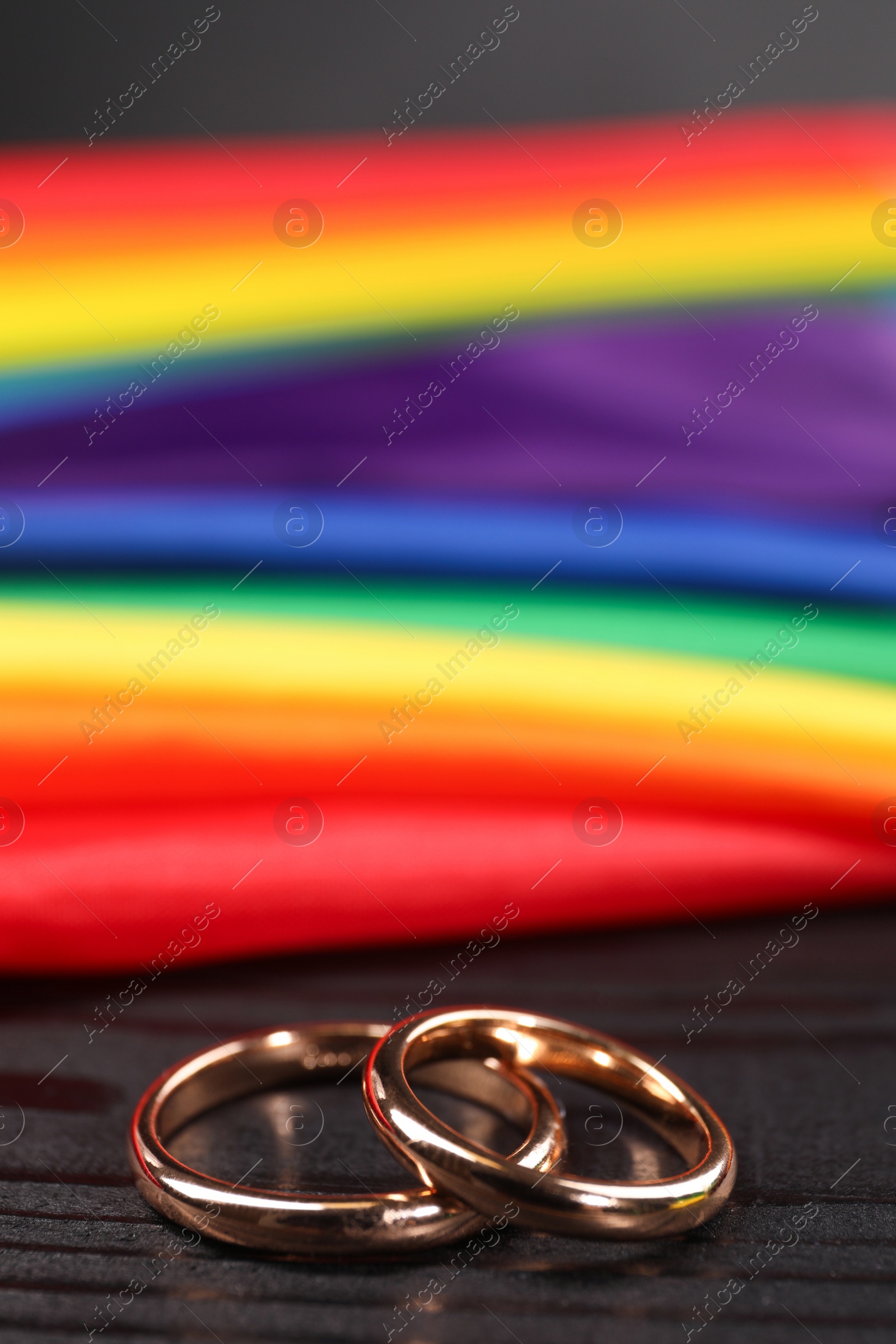 Photo of Rainbow LGBT flag and wedding rings on black wooden background, closeup