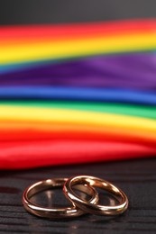 Photo of Rainbow LGBT flag and wedding rings on black wooden background, closeup