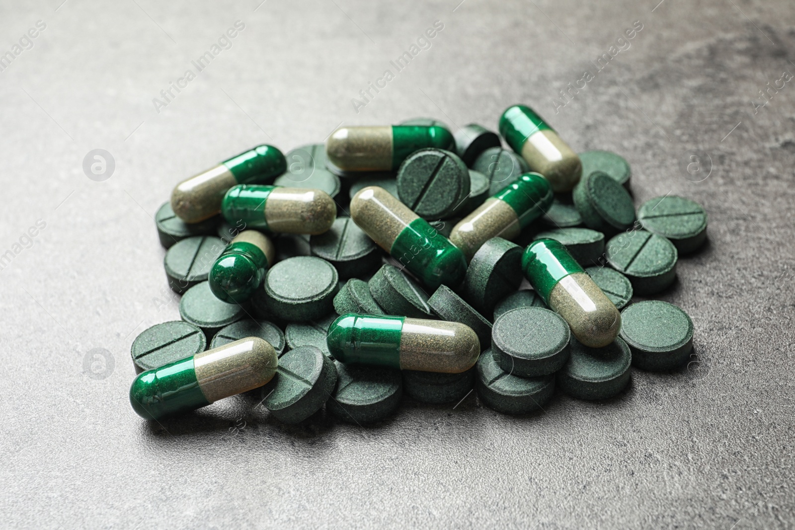 Photo of Green spirulina pills and capsules on color background