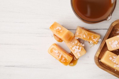 Photo of Yummy caramel candies, sauce and sea salt on white wooden table, top view. Space for text