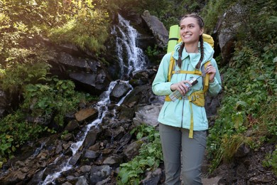 Photo of Tourist with backpack and bottle near waterfall in mountains. Space for text