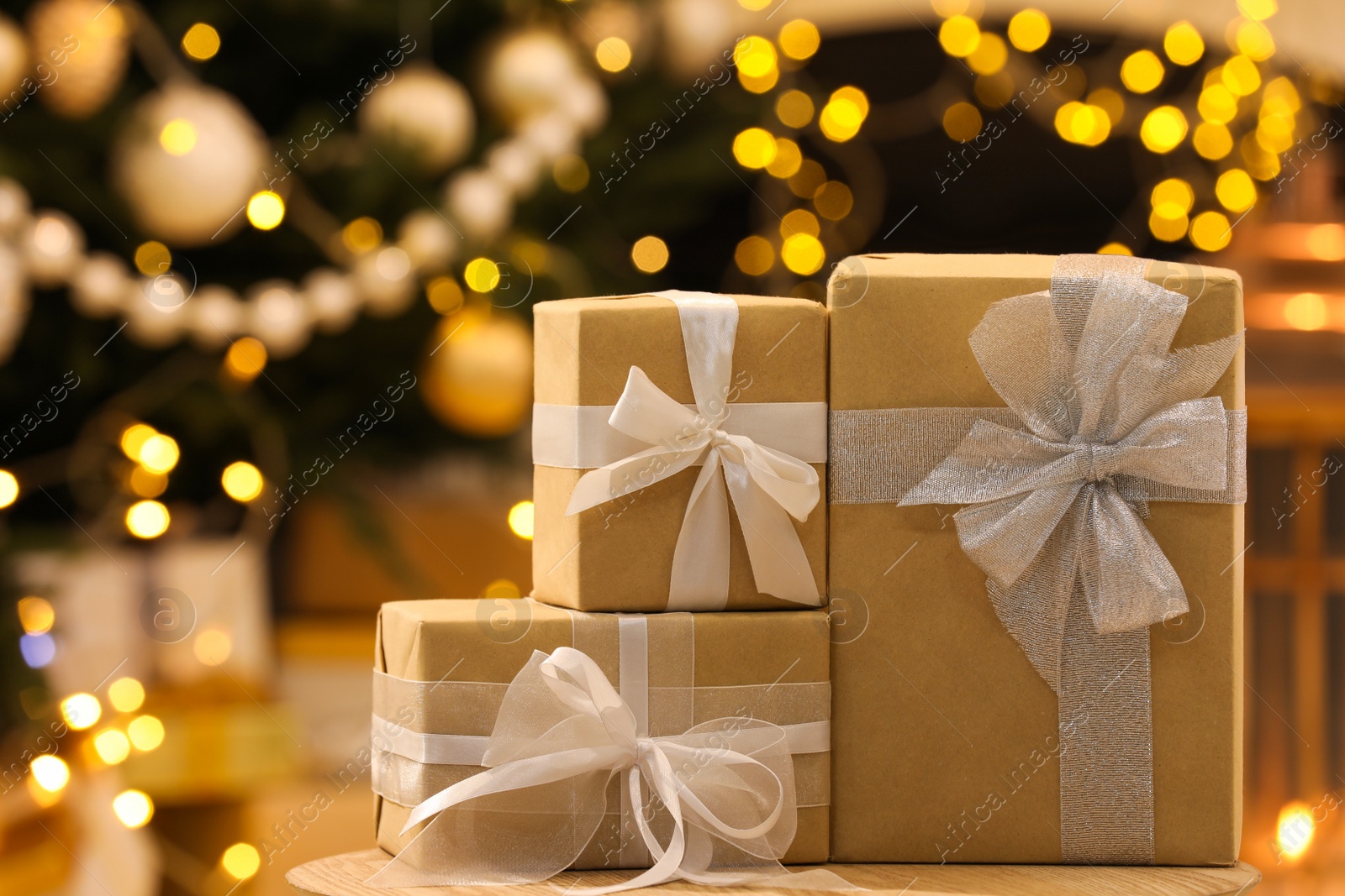 Photo of Beautifully wrapped gift boxes on wooden table against blurred festive lights. Christmas celebration