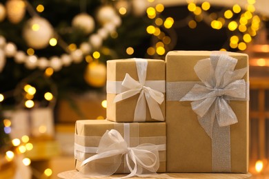 Photo of Beautifully wrapped gift boxes on wooden table against blurred festive lights. Christmas celebration