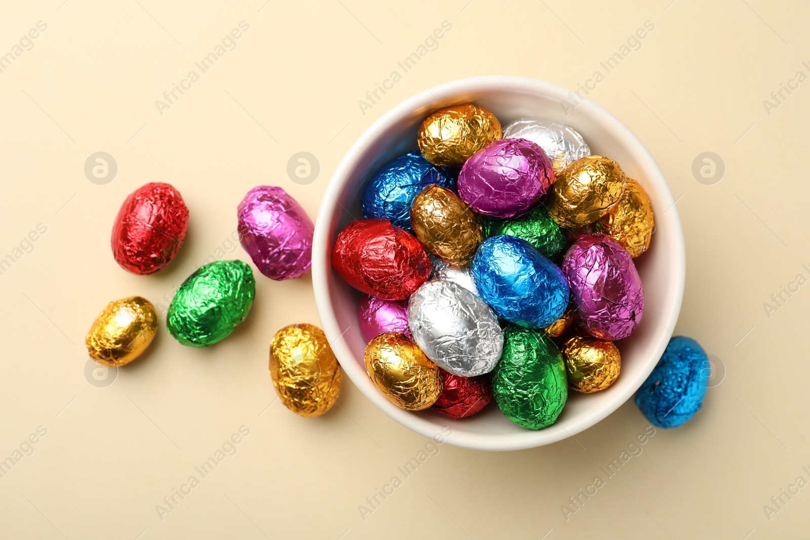 Photo of Chocolate eggs wrapped in colorful foil on beige background, flat lay