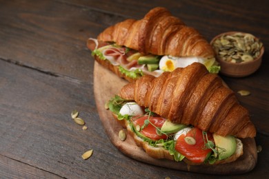 Delicious croissants with salmon and pumpkin seeds on wooden table, space for text