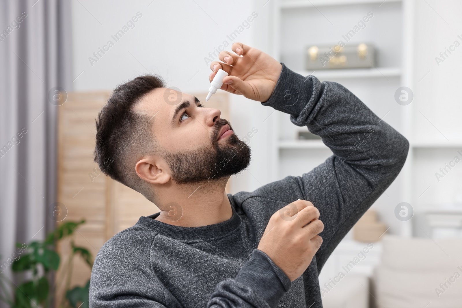 Photo of Young man applying medical eye drops indoors