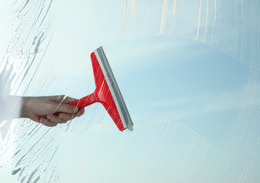 Photo of Woman cleaning window with squeegee on spring day, closeup