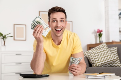 Happy man with money at table in living room