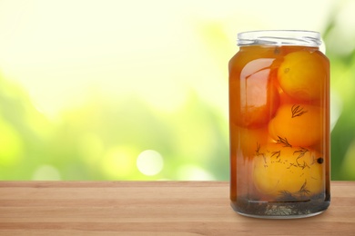 Image of Jar of pickled tomatoes on wooden table against blurred background, space for text