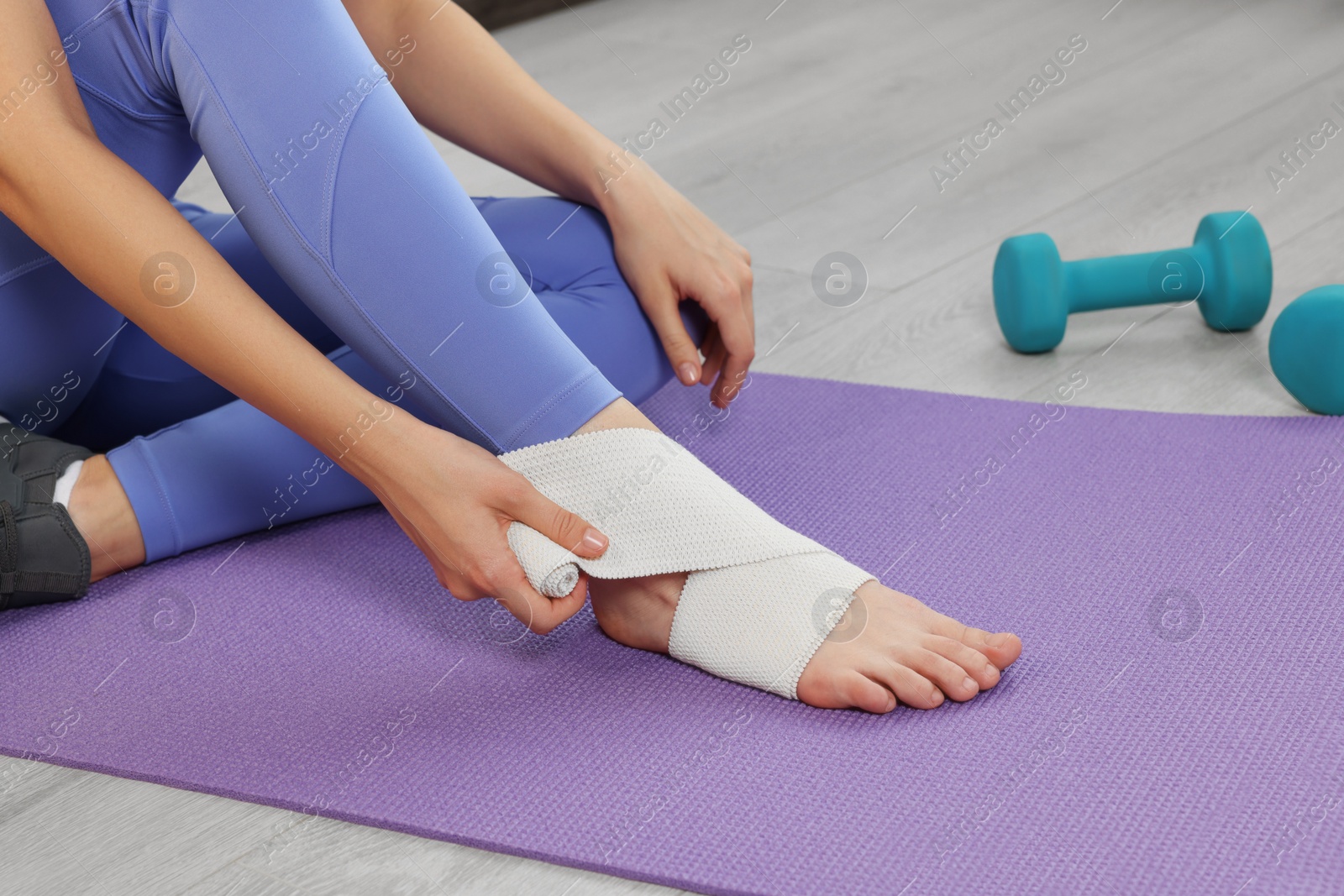 Photo of Woman wrapping foot in medical bandage on yoga mat indoors, closeup