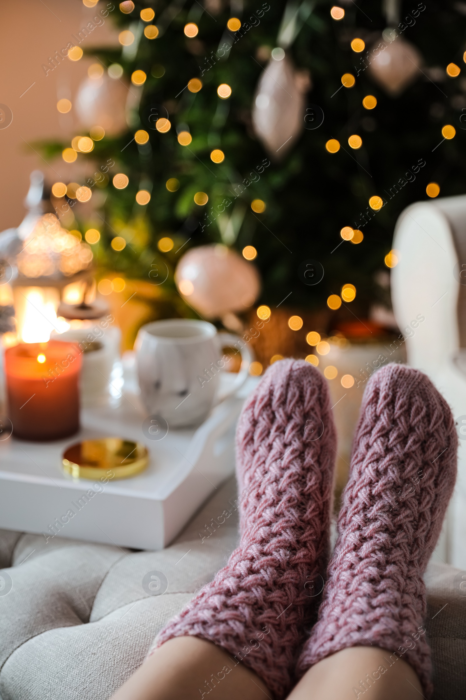 Photo of Woman wearing pink knitted socks in room decorated  for Christmas, closeup