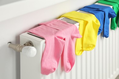 Different colorful socks hanging on white radiator indoors