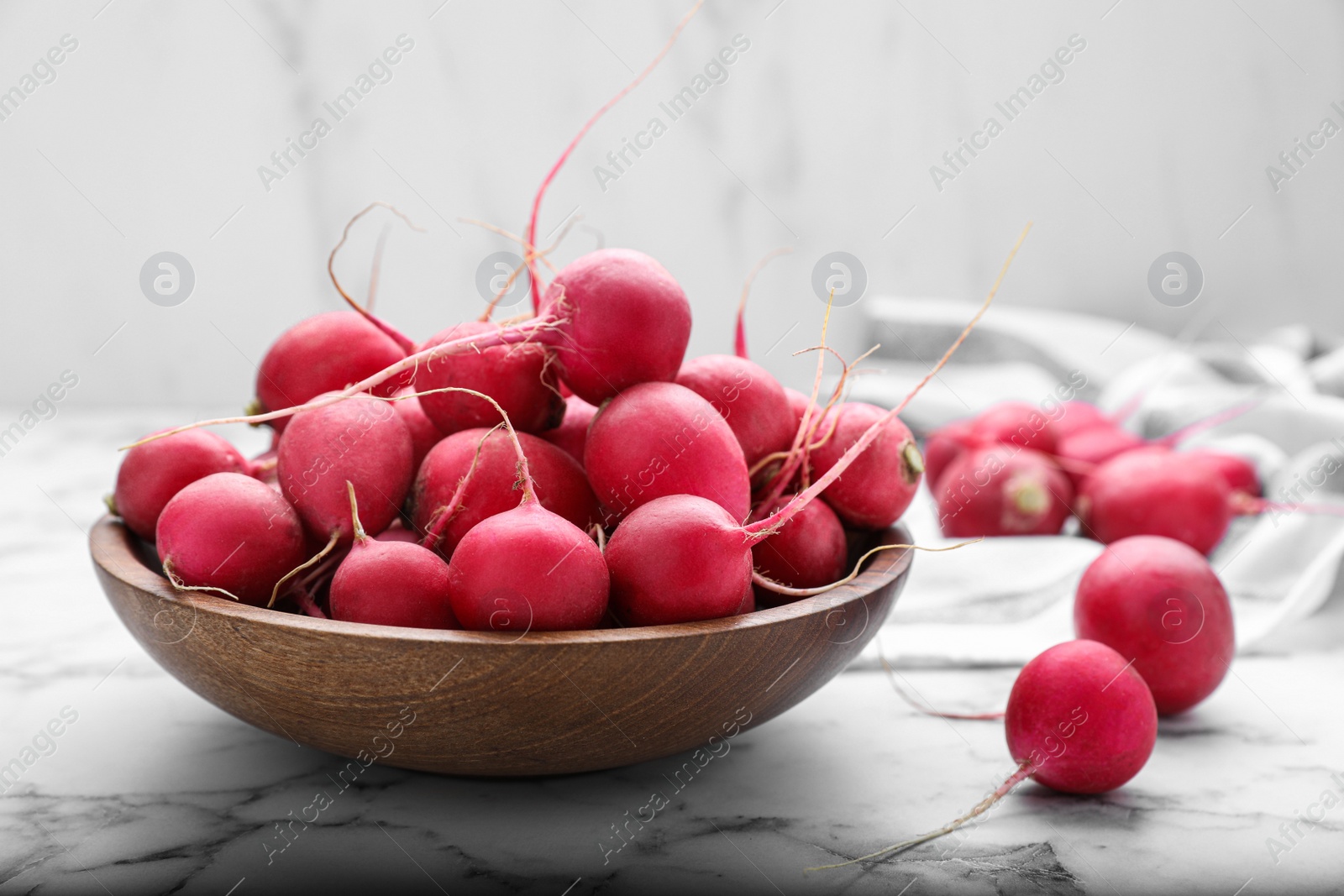 Photo of Bowl with fresh ripe radishes on white marble table, closeup