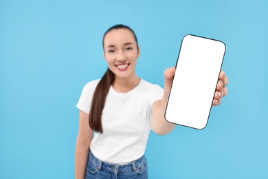 Young woman showing smartphone in hand on light blue background, selective focus. Mockup for design