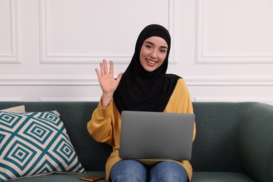 Muslim woman in hijab using laptop on sofa indoors