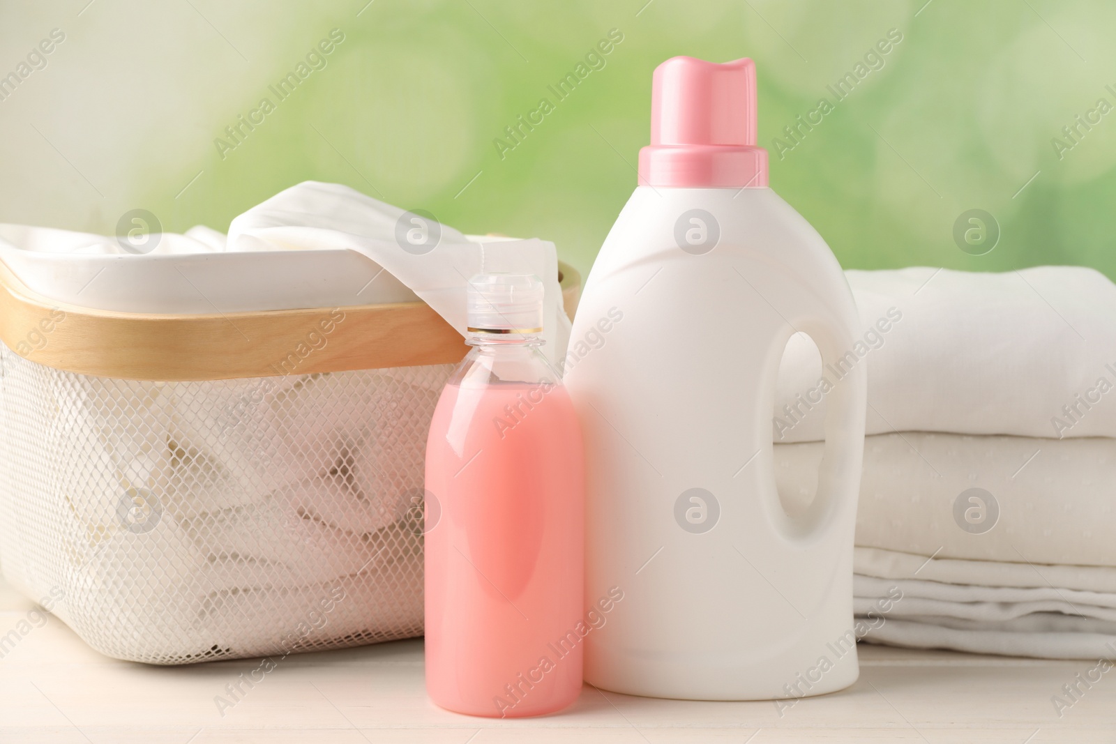 Photo of Bottles of laundry detergents and clean clothes on white wooden table