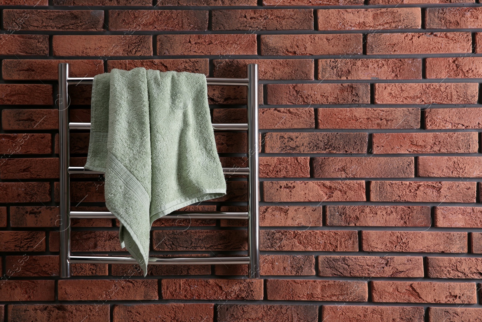 Photo of Modern heated towel rail with warm soft towel on red brick wall. Space for text