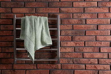 Photo of Modern heated towel rail with warm soft towel on red brick wall. Space for text