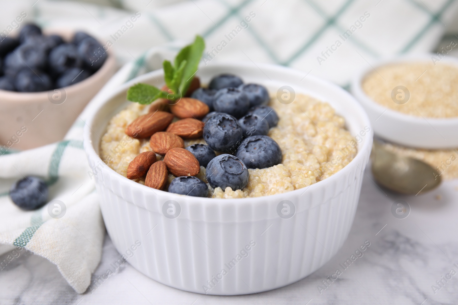 Photo of Bowl of delicious cooked quinoa with almonds and blueberries on white marble table, closeup